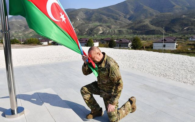 Ilham Aliyev, forseti Aserbaídsjan, krýpur fyrir framan þjóðarfánann. Aserbaídsjanar hafa hrakið nánast alla Armena sem …