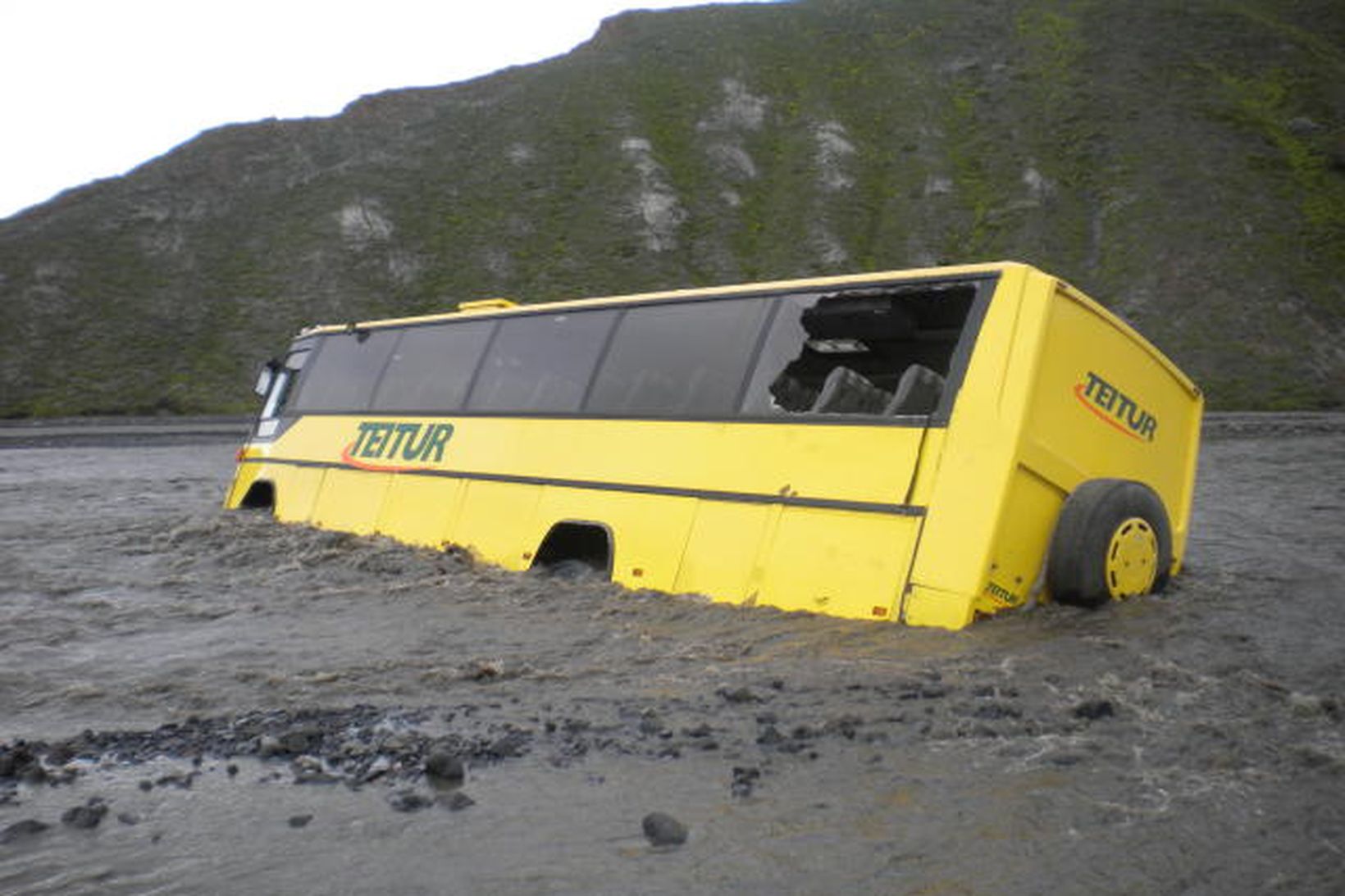 Rútan í ánni eftir að börnunum hafði verið bjargað út.