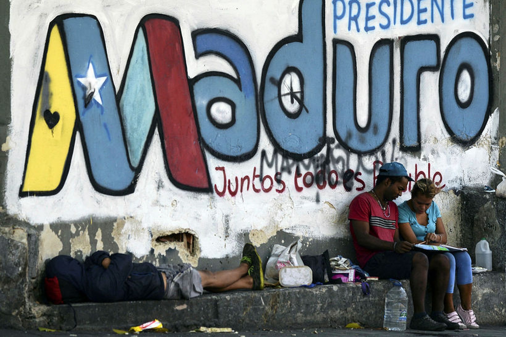 Fólk hvílir lúin bein undir veggjakroti til stuðnings Nicolas Maduro …