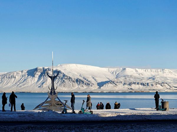 Tourists by the sculpture The Sun Voyager by Jón Gunnar Árnason by Sæbraut in Reykjavík facing Mt Esja and the open sea.
