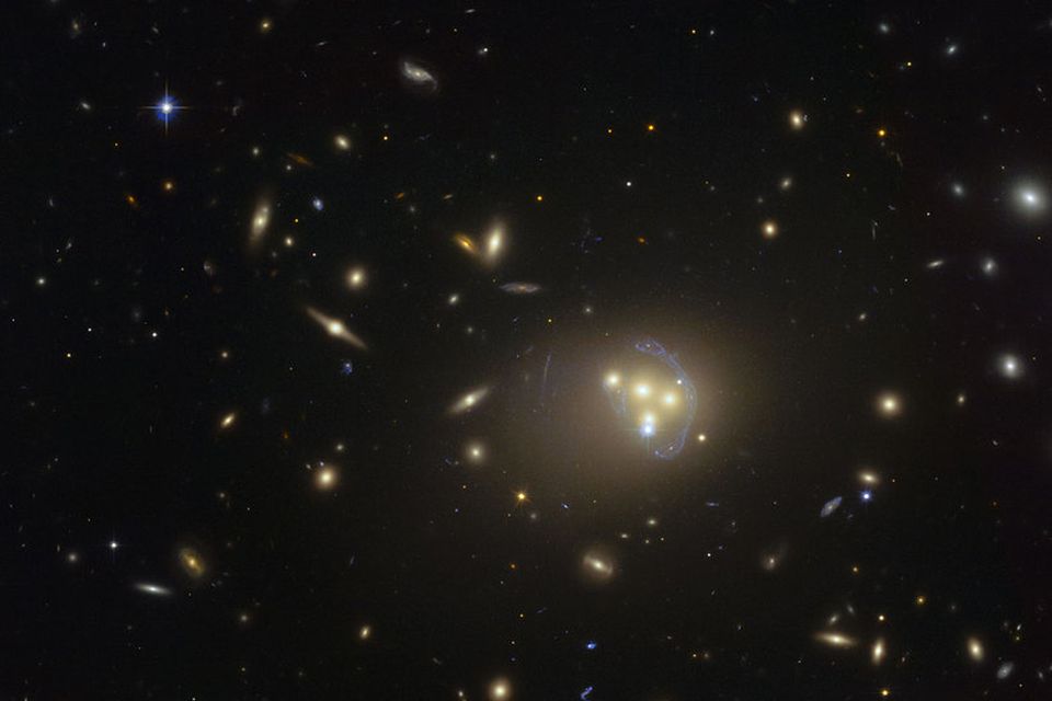 Mynd Hubble-geimsjónaukans af vetrarbrautaþyrpingunni Abell 3827. Bláa slykjan utan um vetrarbrautirnar á miðri myndinni er …