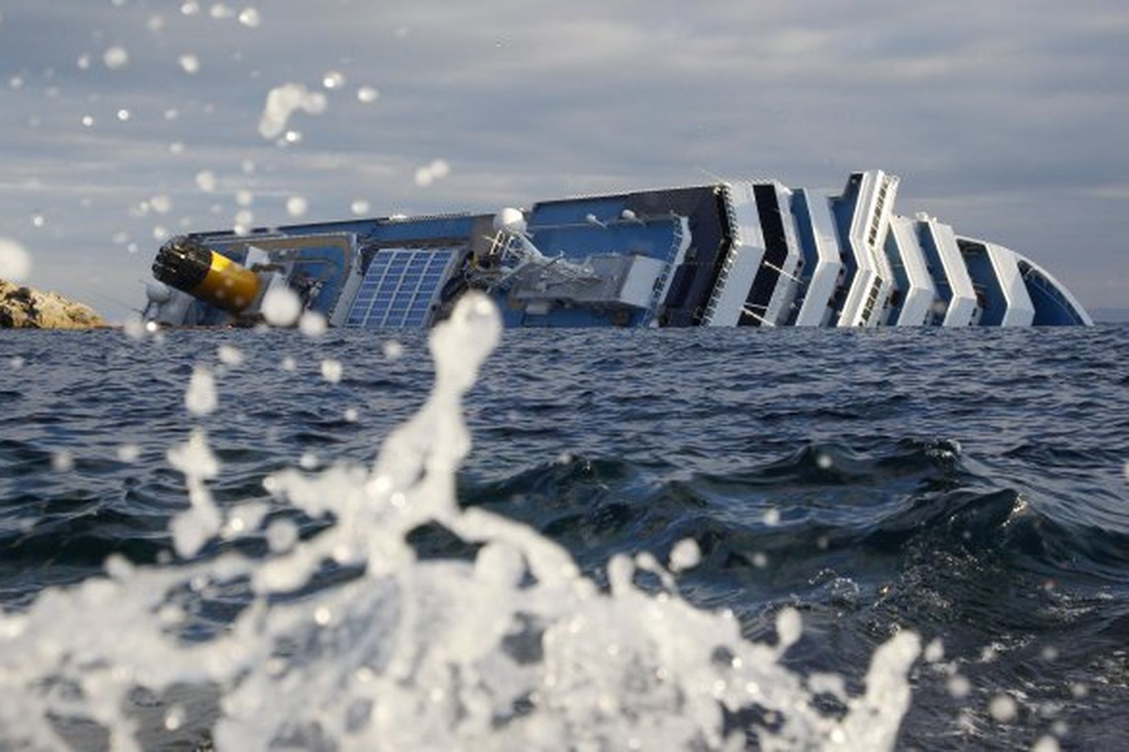 Costa Concordia liggur á hliðinni við ströndina.