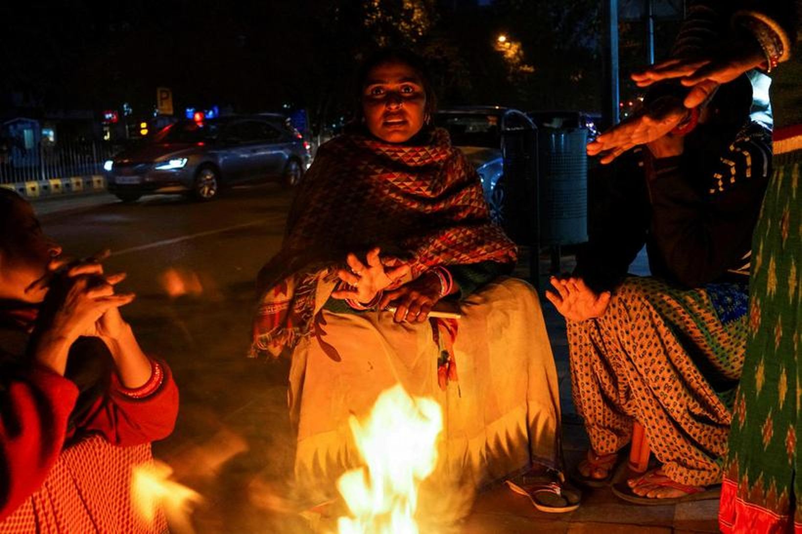 Indverskar konur sitja við varðeld á köldu kvöldi í Delhi. …