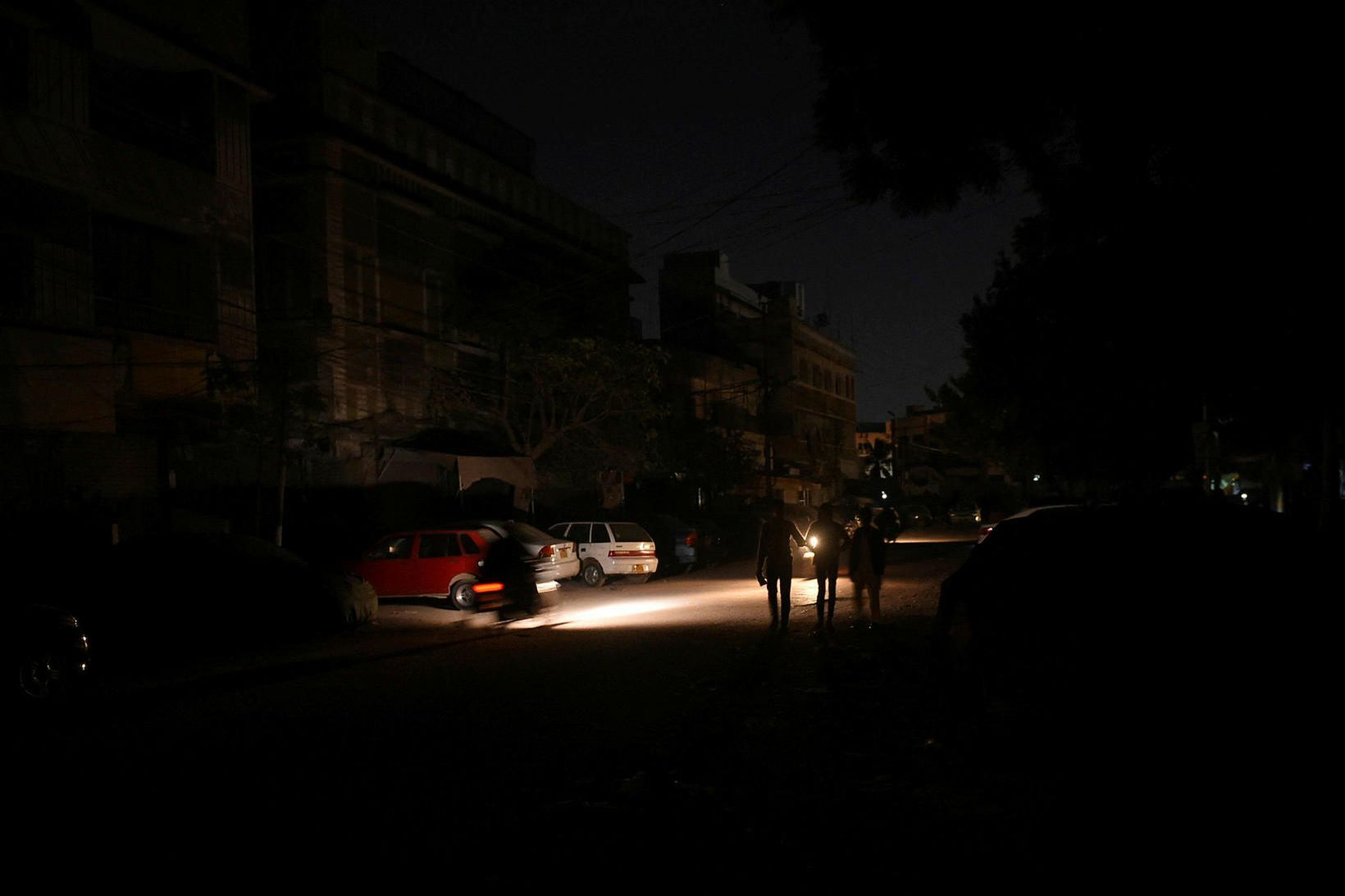Fólk gengur um stræti Karachi, fjölmennustu borgar Pakistans, í niðamyrkri.