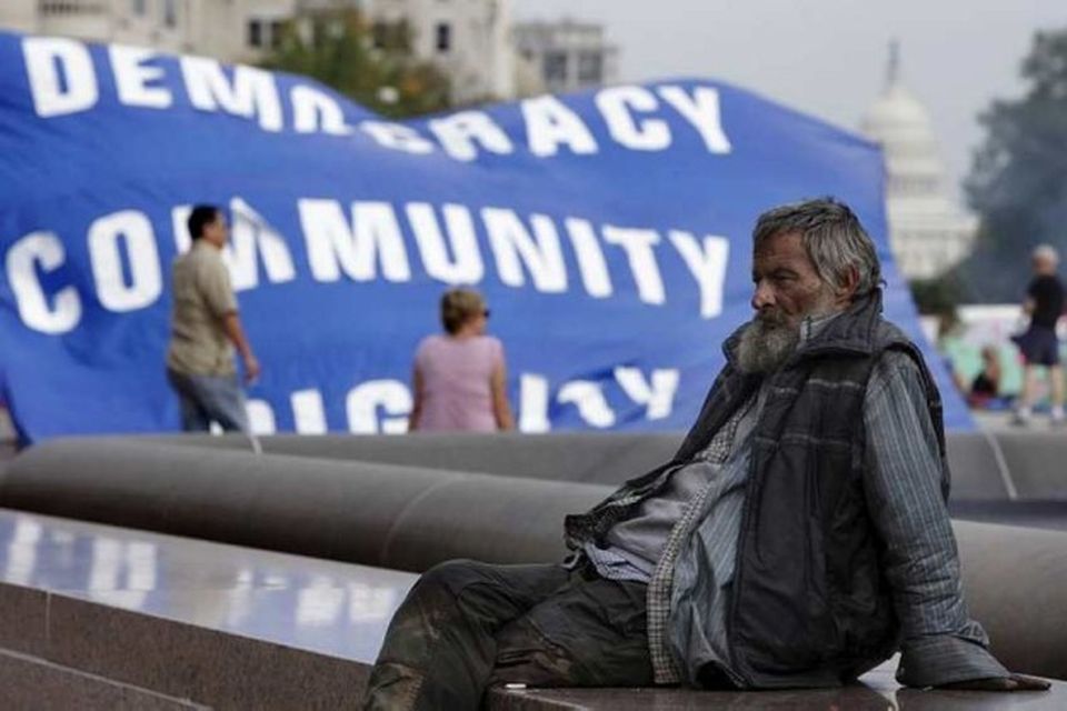 REFILE - CLARIFYING CAPTIONA man sits in front of a banner of the Occupy D.C …