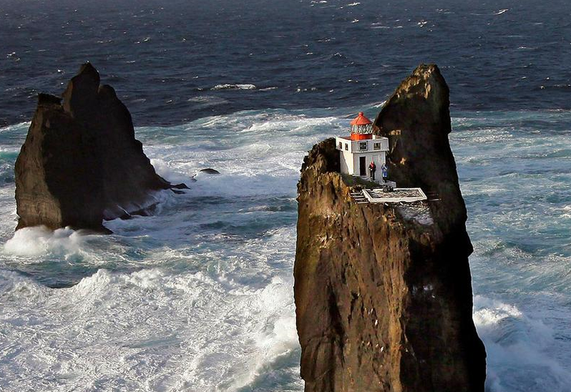 The lighthouse is surrounded by open water and is precariously perched on a cliff.