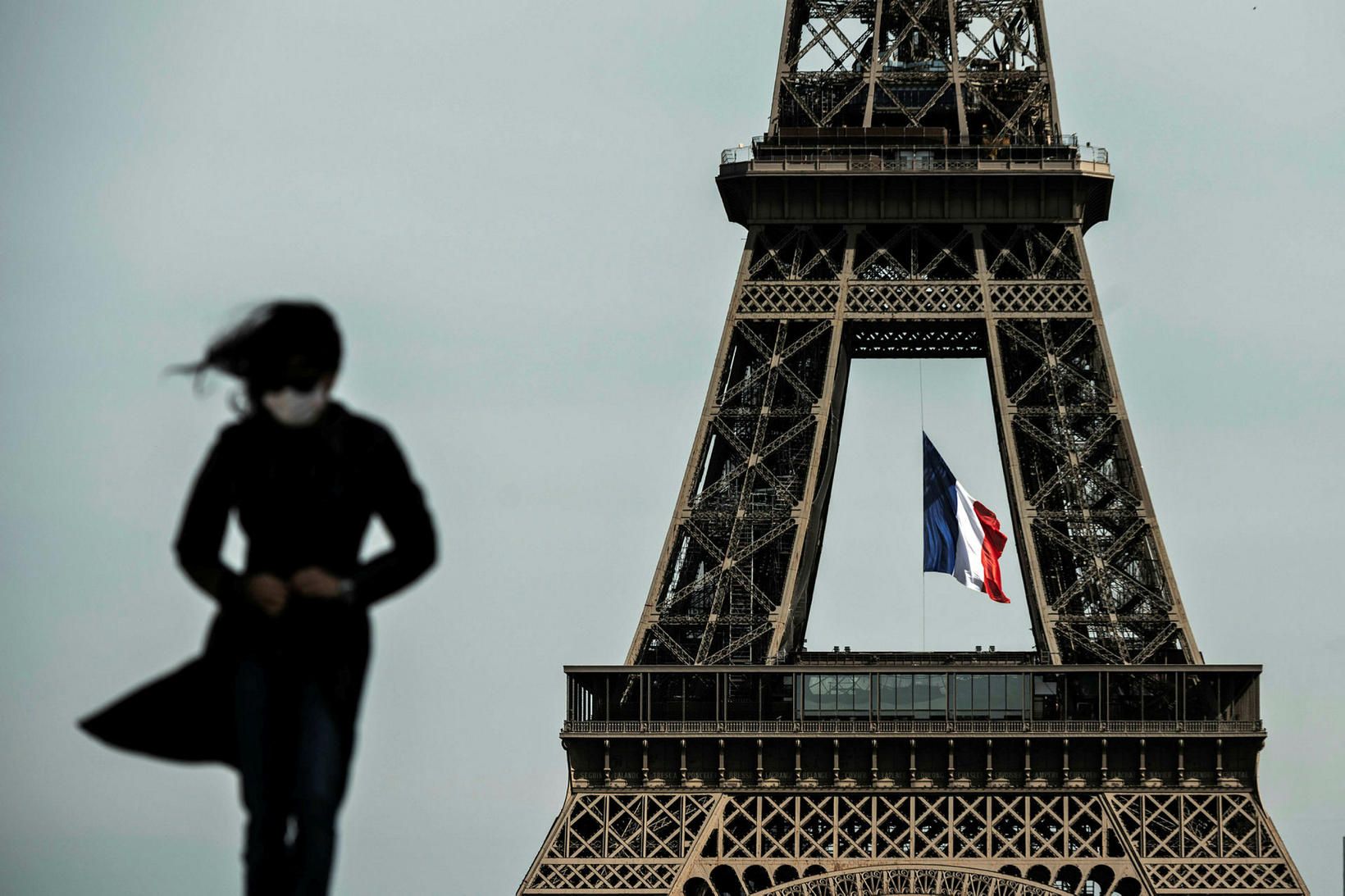 Kona með grímu við Eiffel-turn­inn í París.