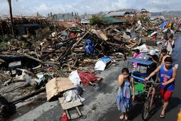 Eftirlifendur náttúruhamfaranna ganga fram hjá húsarústum og rotnandi líkum í Tacloban.