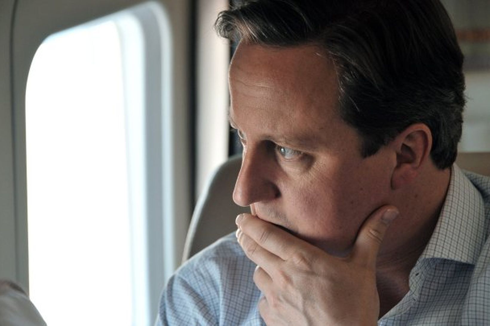 David Cameron horfir íbygginn út um glugga flugvélar. Mynd úr …