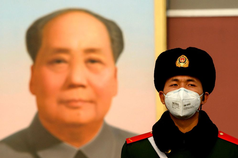 A soldier in Beijing, in front of a poster of Mao Zedong.