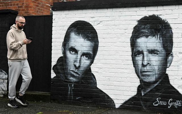 Vegfarandi sést hér ganga fram hjá veggmynd af bræðrunum Liam og Noel Gallagher, sem eru …