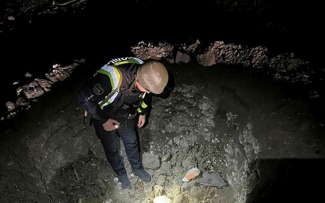 Lögreglumaður skoðar gíg í húsagarði íbúðarhúss eftir eldflaugaárásir Rússa á Kænugarð í nótt.