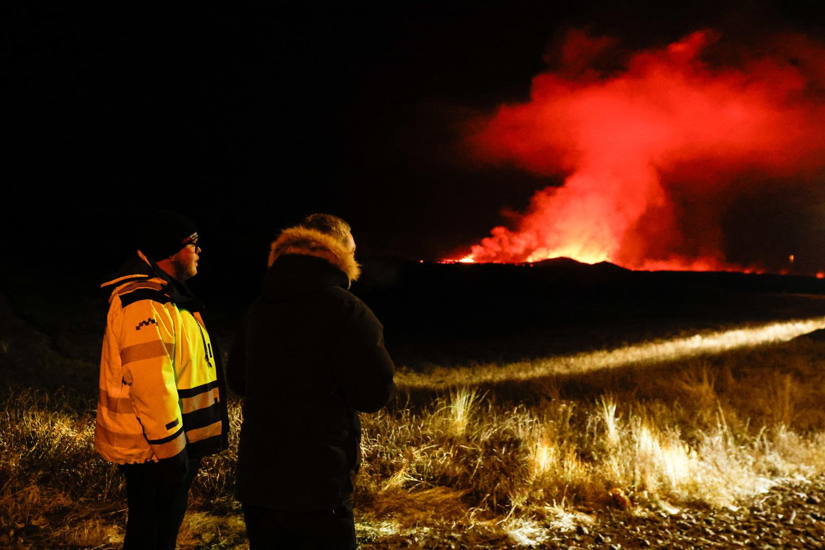 Viðbragðsaðli ásamt ferðamanni við Grindavíkurveg virða fyrir sér gosið nú …