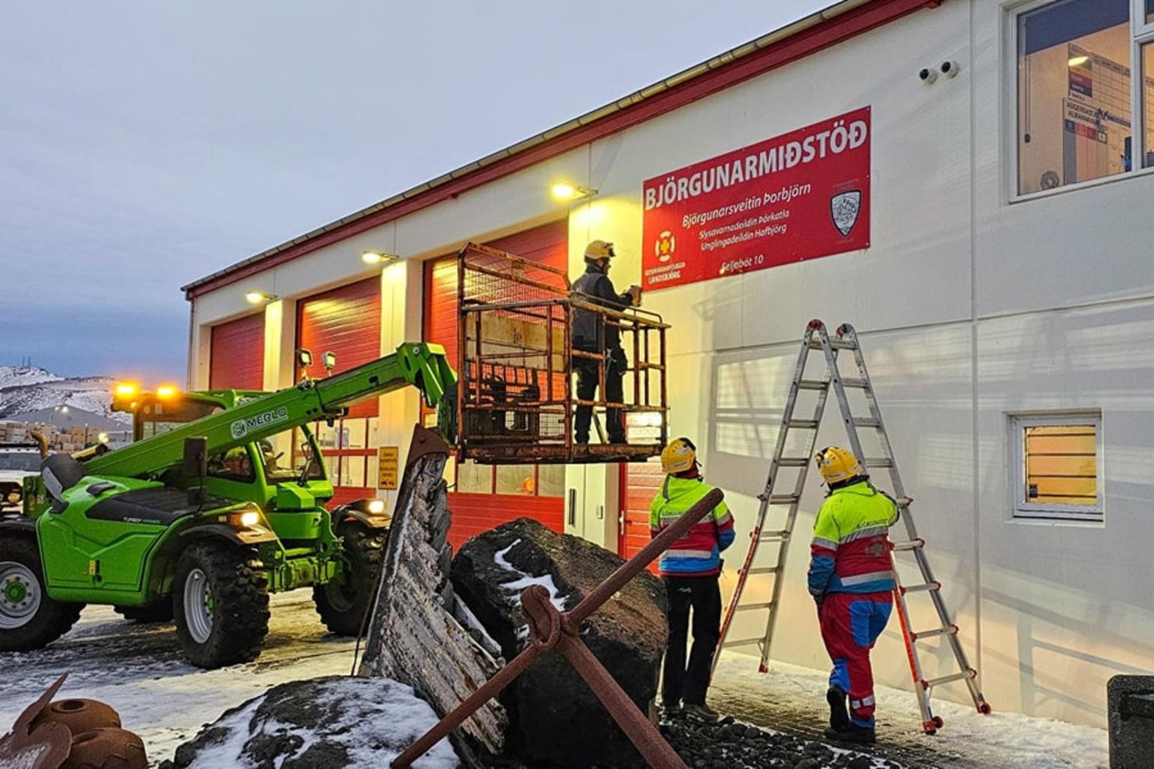 Björgunarsveitarmenn fylgjast með þegar nýtt skilti er sett upp á …