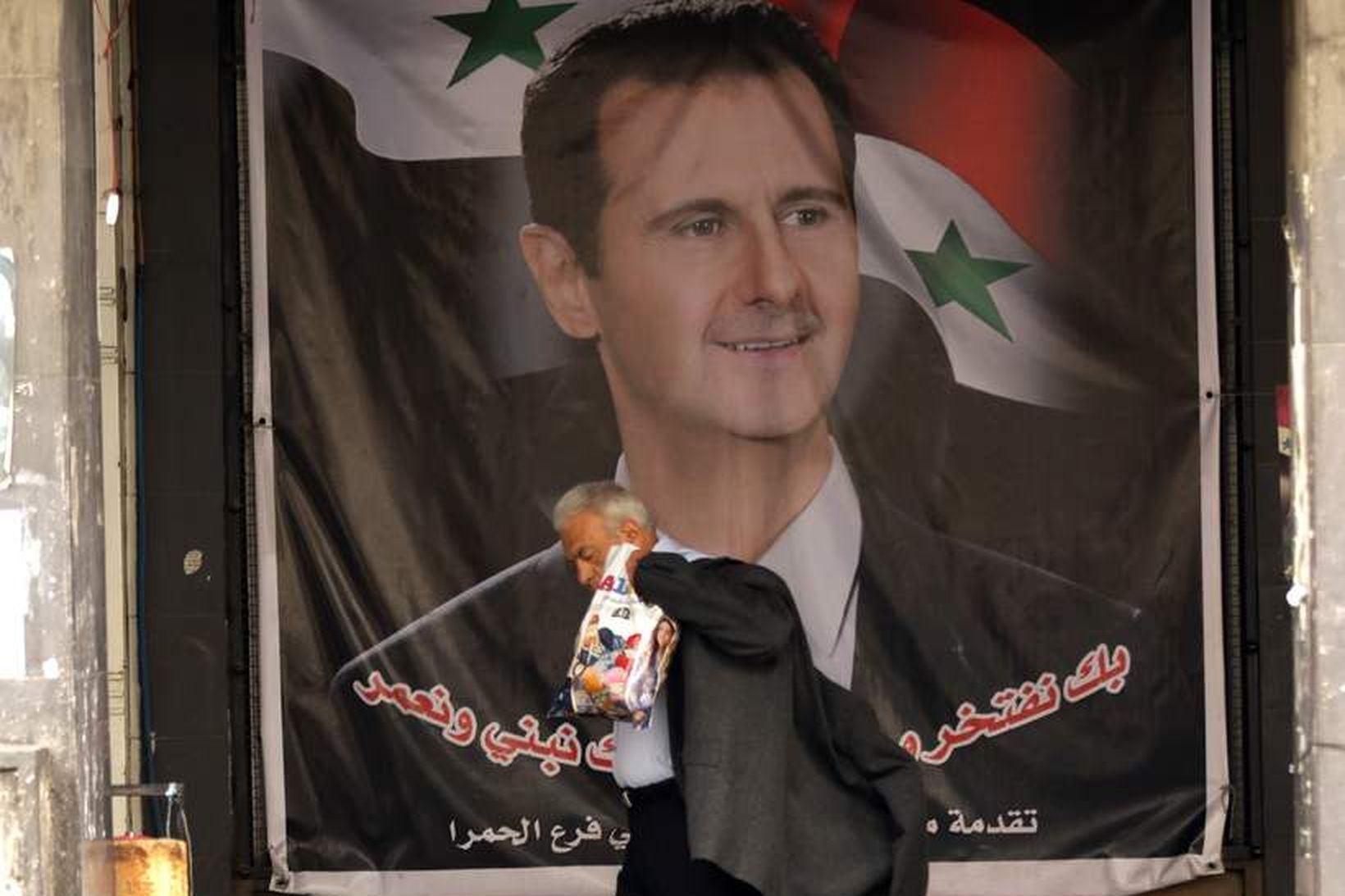 Sýrlenskur maður gengur framhjá mynd af Assad, forseta Sýrlands í …