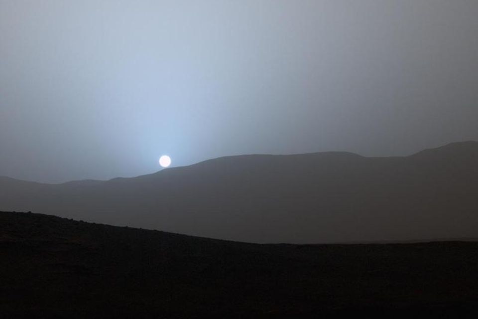 Bláleit sólin sest til viðar í hæðunum í kringum könnunarjeppann Curiosity á mars.