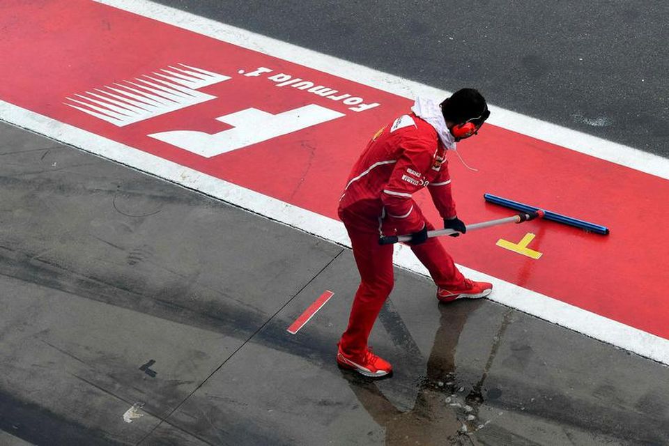 Liðsmaður Ferrari ýtir vatni burt frá bílskúr liðsins fyrir tímatökuna í Monza.
