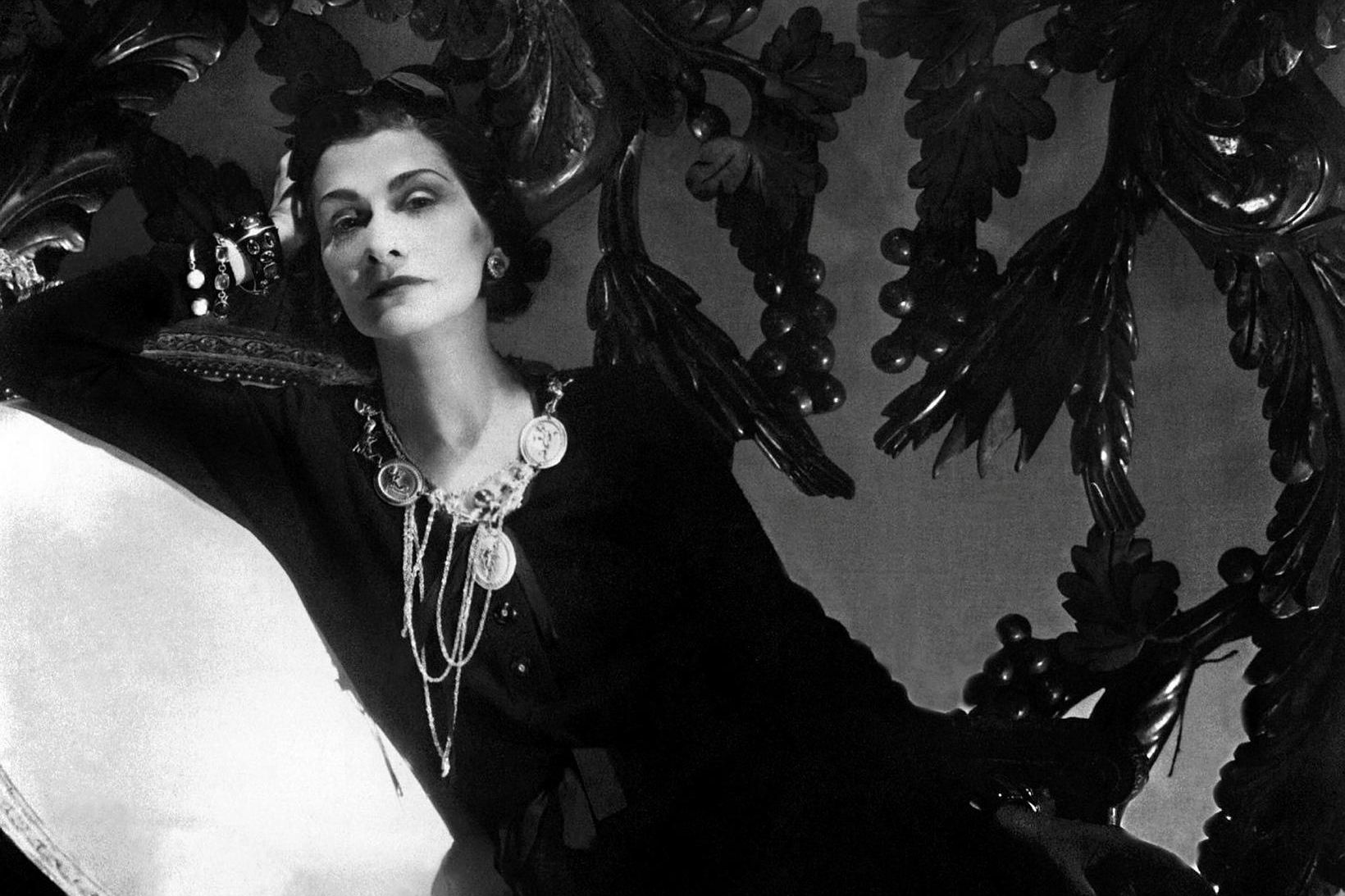 Hér er Coco Chanel í hvíta stólnum árið 1944. Myndin …